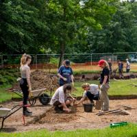 Archaeology students working at an excavation site with wheelbarrows and spades