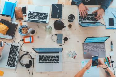 Image of a desk with lots of different media and devices, like laptops, cameras, mobile phones, headphones, and more.