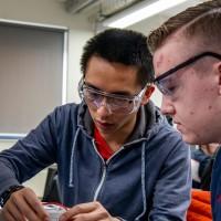 Two male undergraduate electronic engineering students with goggles adjusting device