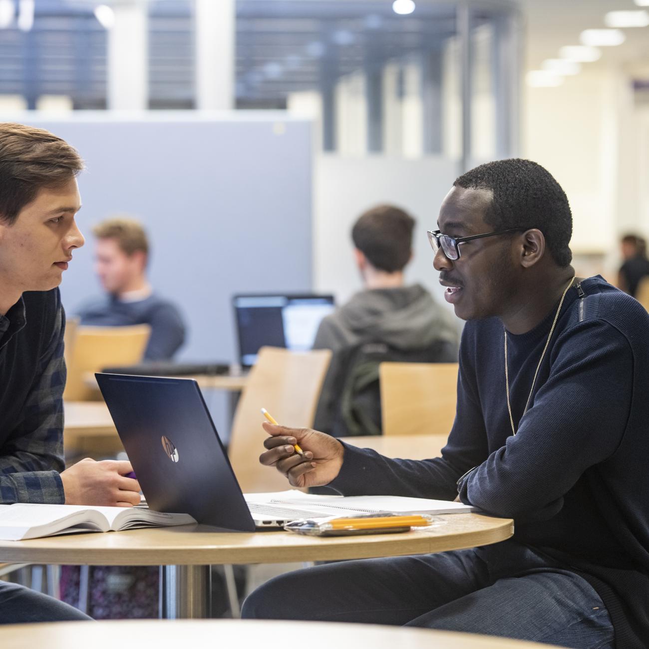 2 men in discussion at a table with laptop.