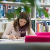 A female student studying various texts at a desk in the library