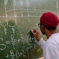 A person with their back to us works out a maths equation on a chalkboard