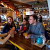 Group of students sat at table in a restaurant bar, talking and laughing over drinks.