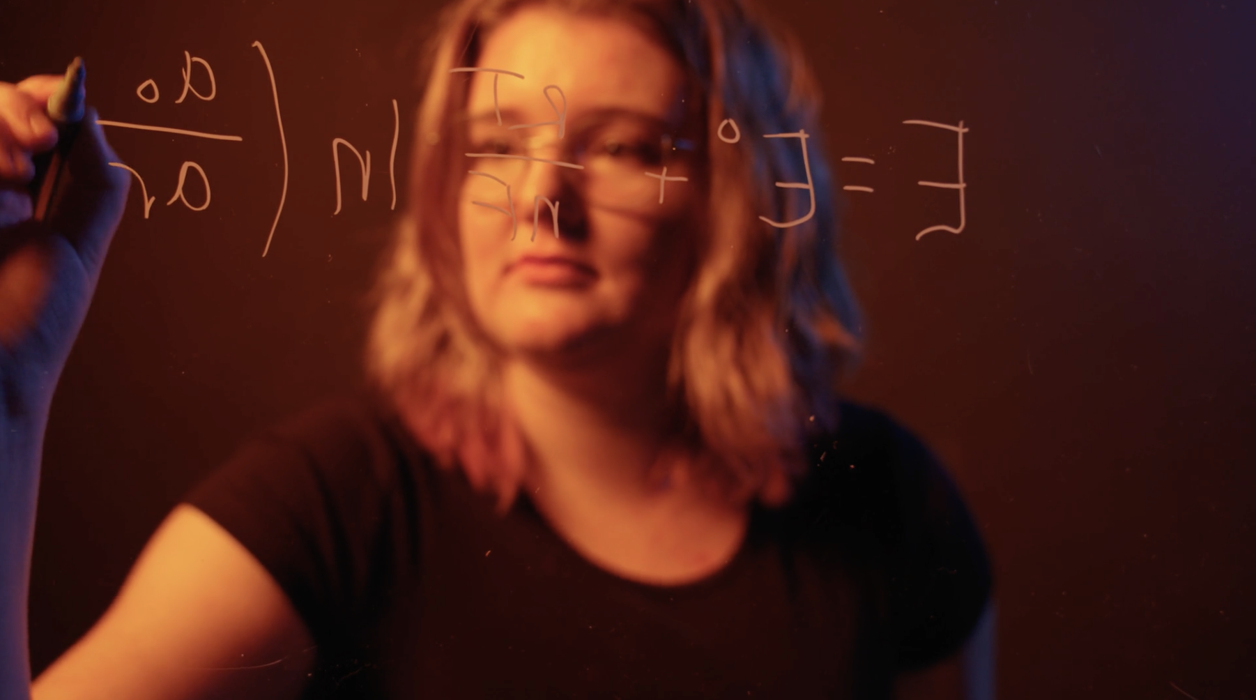 A student writing an equation on a pane of glass.