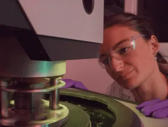 A student wearing protective goggles, gloves and a laboratory coat while operating machinery.