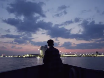 A student on board a boat looks out to a city from across the water.