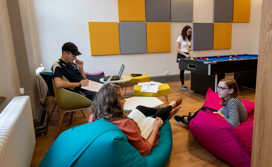 Group of students in common room, sat talking and playing pool.